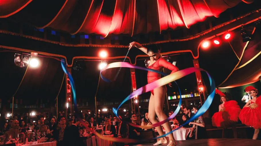 Performer in red with ribbons on stage under tent.