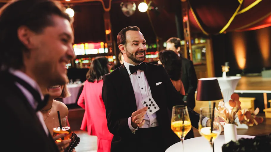 Man in tuxedo performs card trick at event.