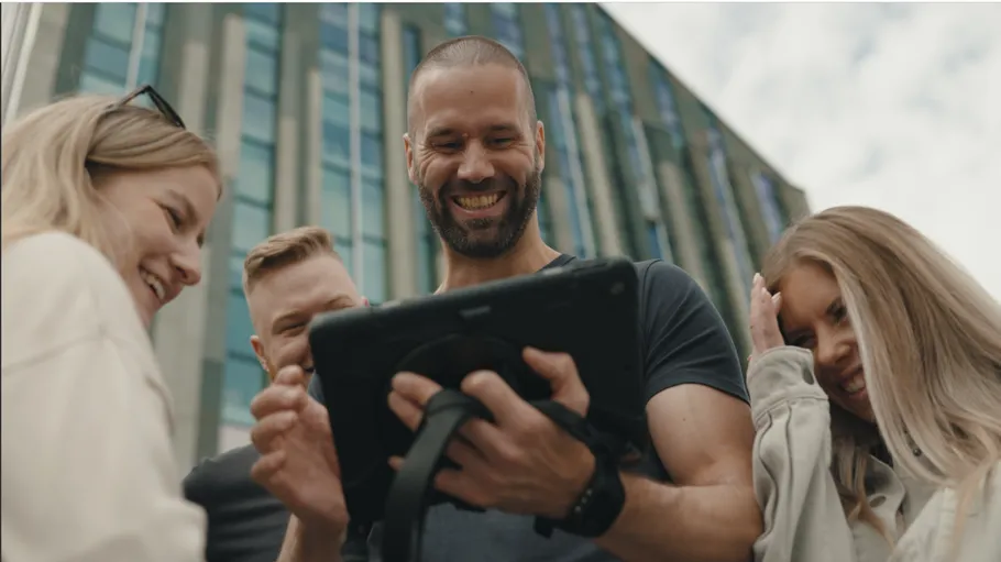Group smiling at tablet, building background.