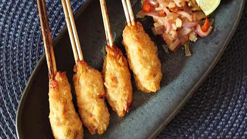 Four skewers of meat with sliced vegetables.