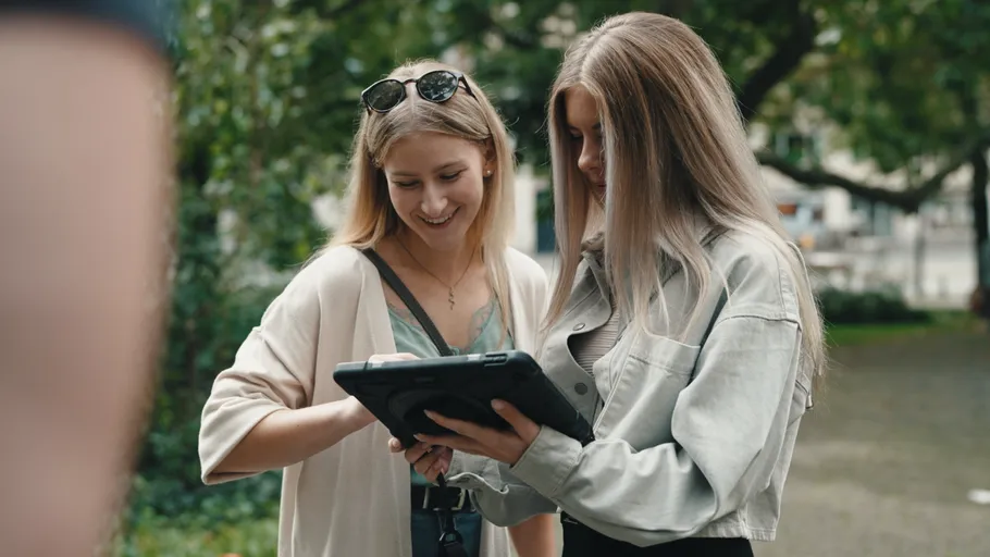Zwei Frauen betrachten ein Tablet im Freien.