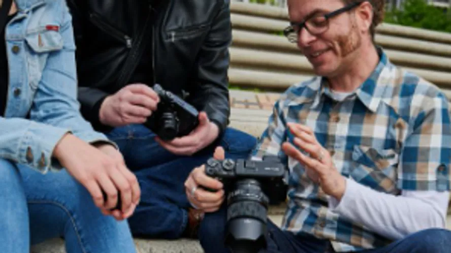 People sitting, holding cameras, discussing in park.