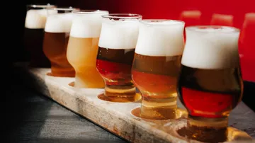 Glasses of beer on a wooden tray, red background.