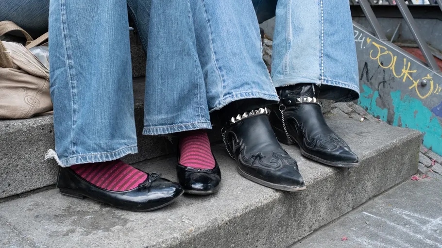 Zwei Schuhpaare, Jeans, auf Treppen sitzend.