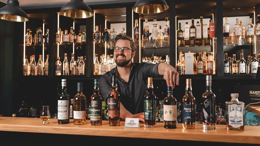 Man smiling behind a bar with various liquor bottles.