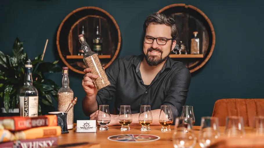 Mann hält Flasche, sitzt am Tisch, Gläser angeordnet.