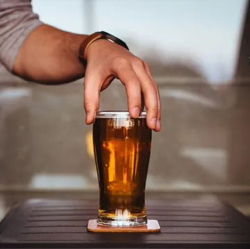 Hand reaching for a glass of beer indoors.