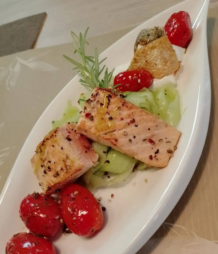 Grilled salmon with tomatoes and cucumber, garnished beautifully.