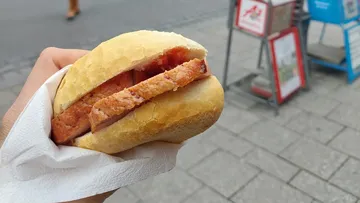 Hand hält Sandwich auf einer Straße.
