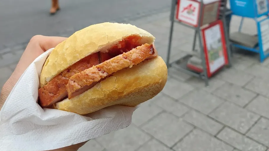 Hand hält Sandwich auf einer Straße.