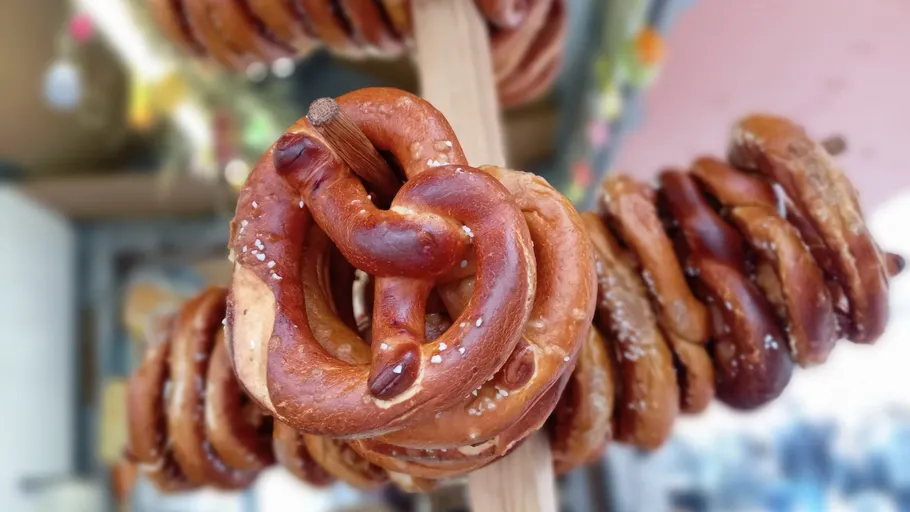 Pretzels hanging on wooden stick outdoors.