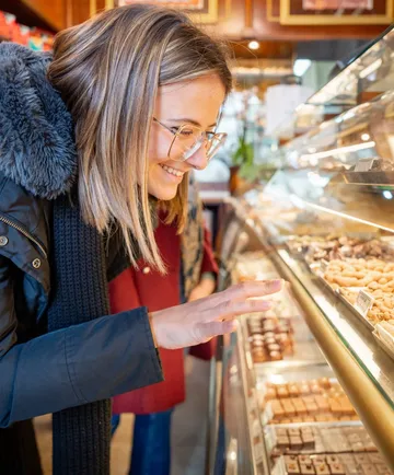 Woman browsing pastries in bakery display.