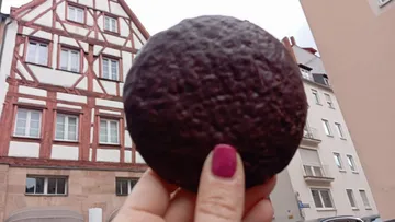 Hand holding a dark cookie in front of building.