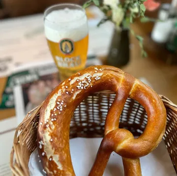 Pretzel in basket, beer in background, table setting.
