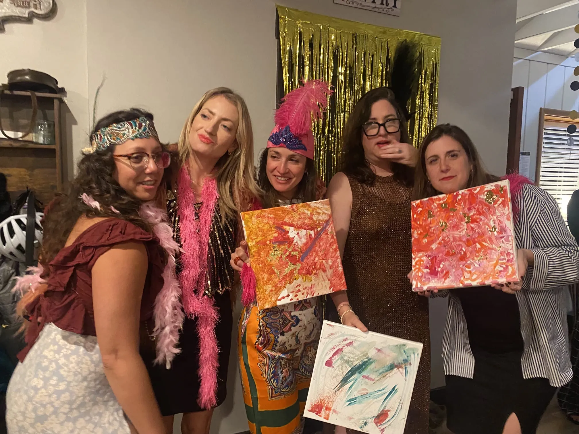 Fünf Frauen posieren mit bemalten Leinwänden drinnen.