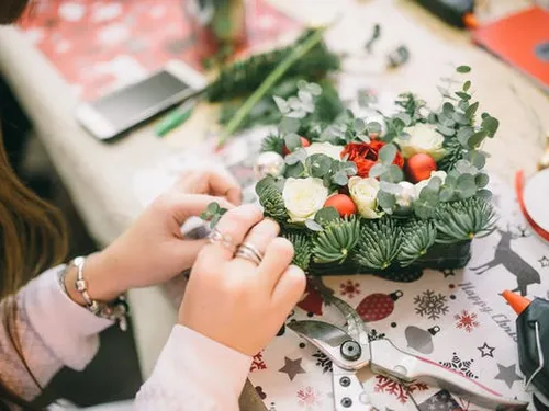 A person creates a festive floral decoration on a table.