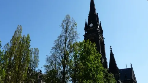 Hoher Kirchturm mit Bäumen daneben.