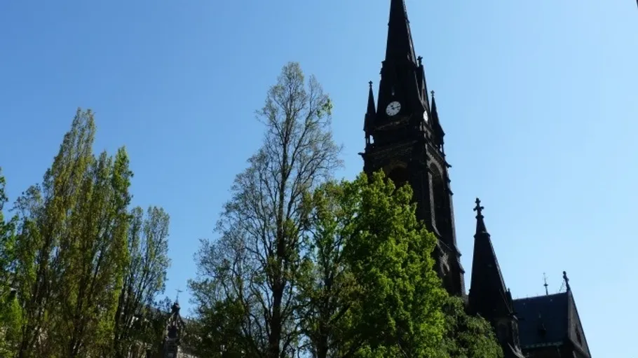 Hoher Kirchturm mit Bäumen daneben.