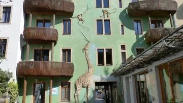Green building with giraffe mural and animal sculptures.