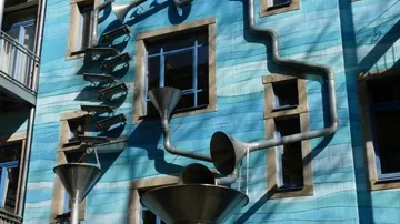 Blaues Gebäude mit künstlerischen Abflussrohren.
