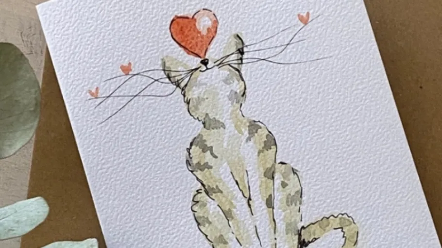 Painted cat looks at heart topping its head.