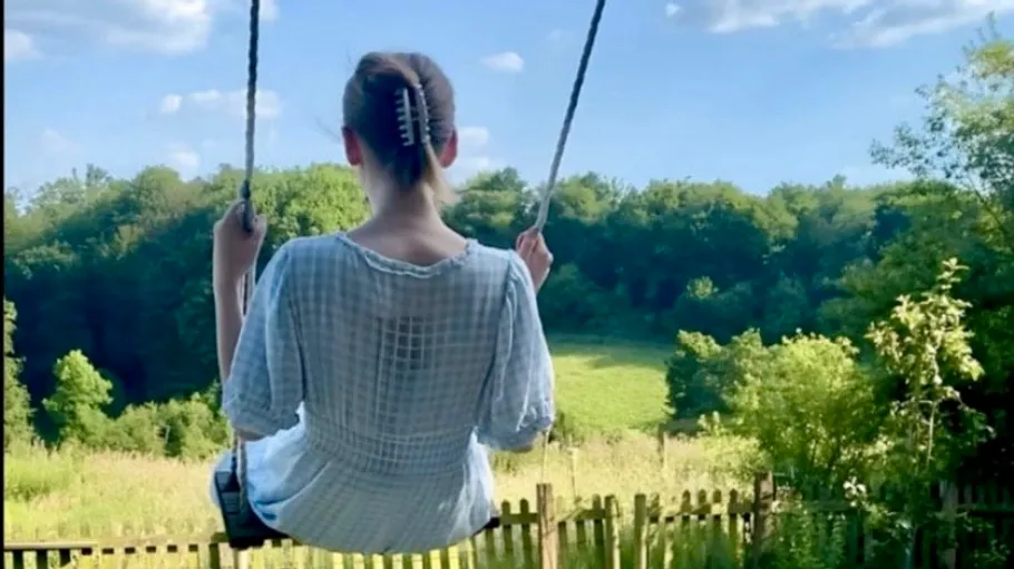 Person on swing overlooking green field and trees.
