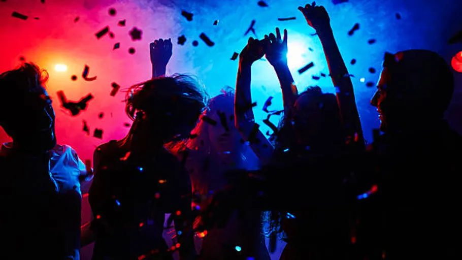 People dancing with confetti under colorful lights.