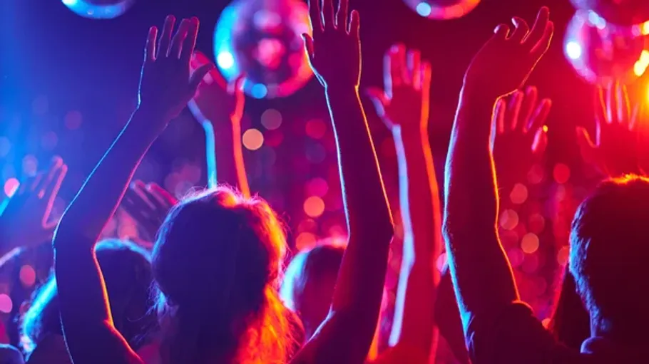 People raising hands under colorful lights.