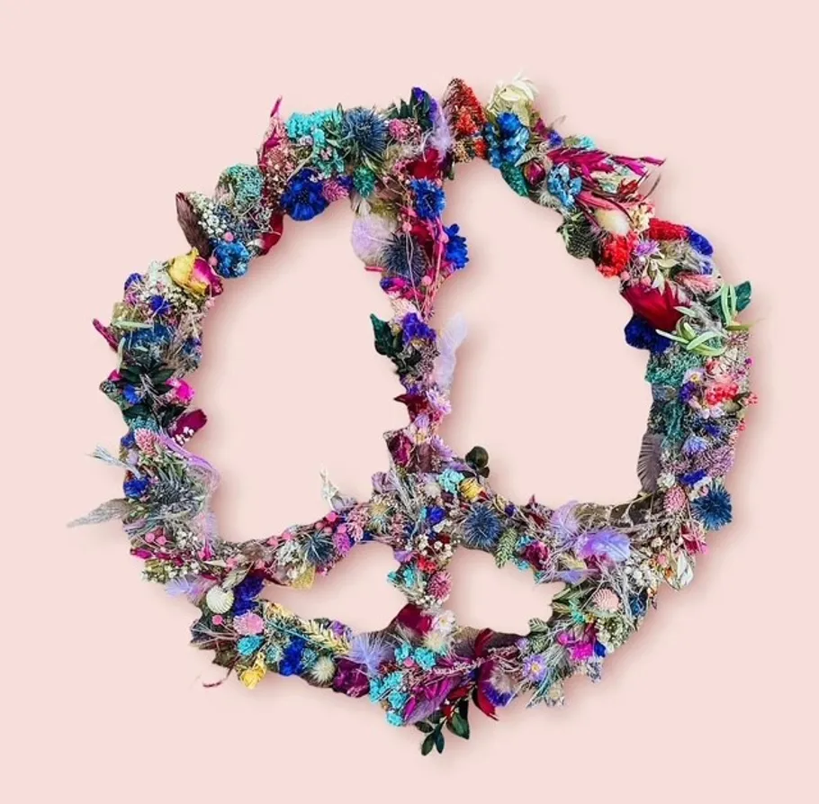 Peace symbol made of colorful flowers, pink background.