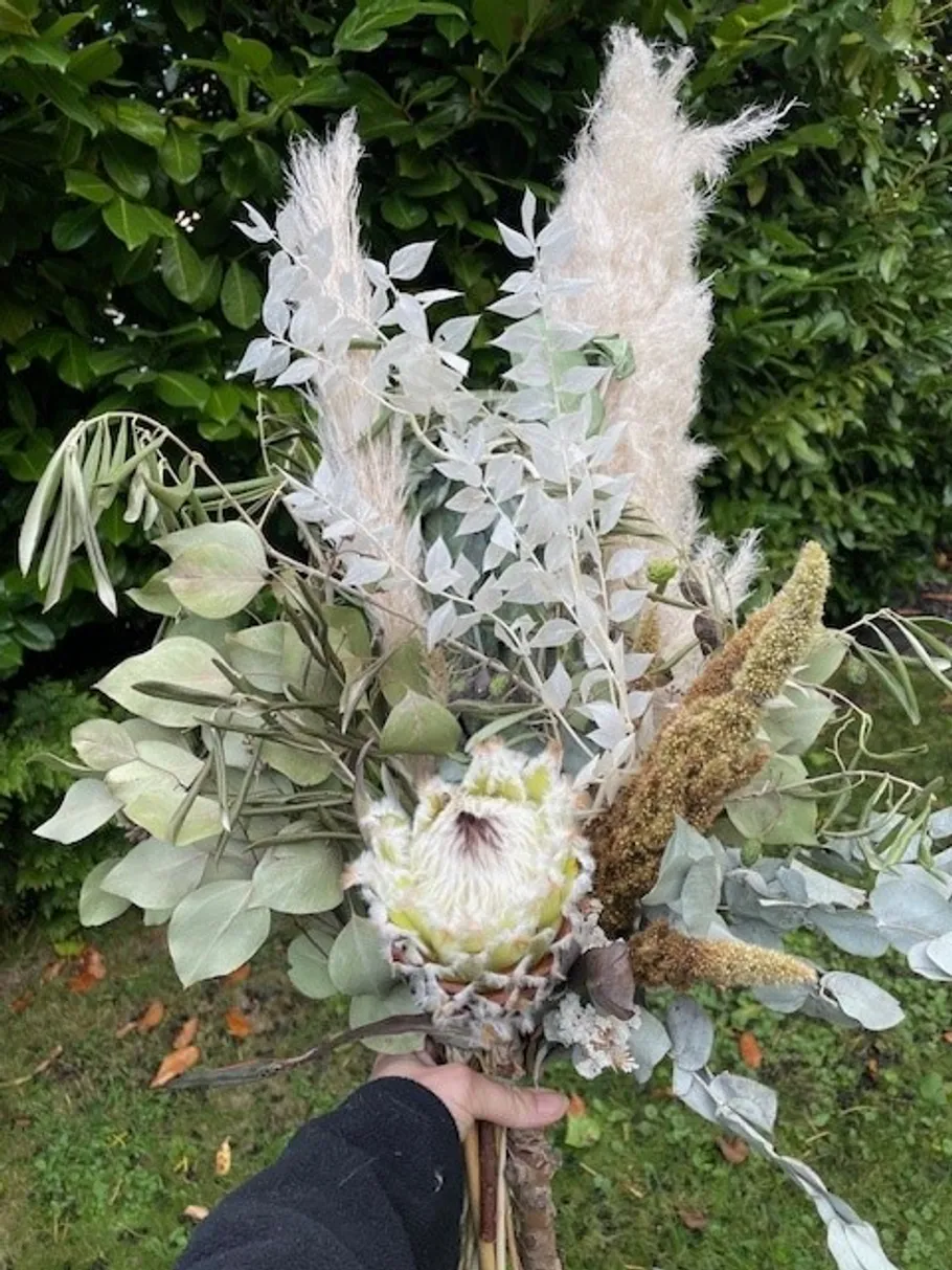 Hand holding bouquet with greenery and pampas.