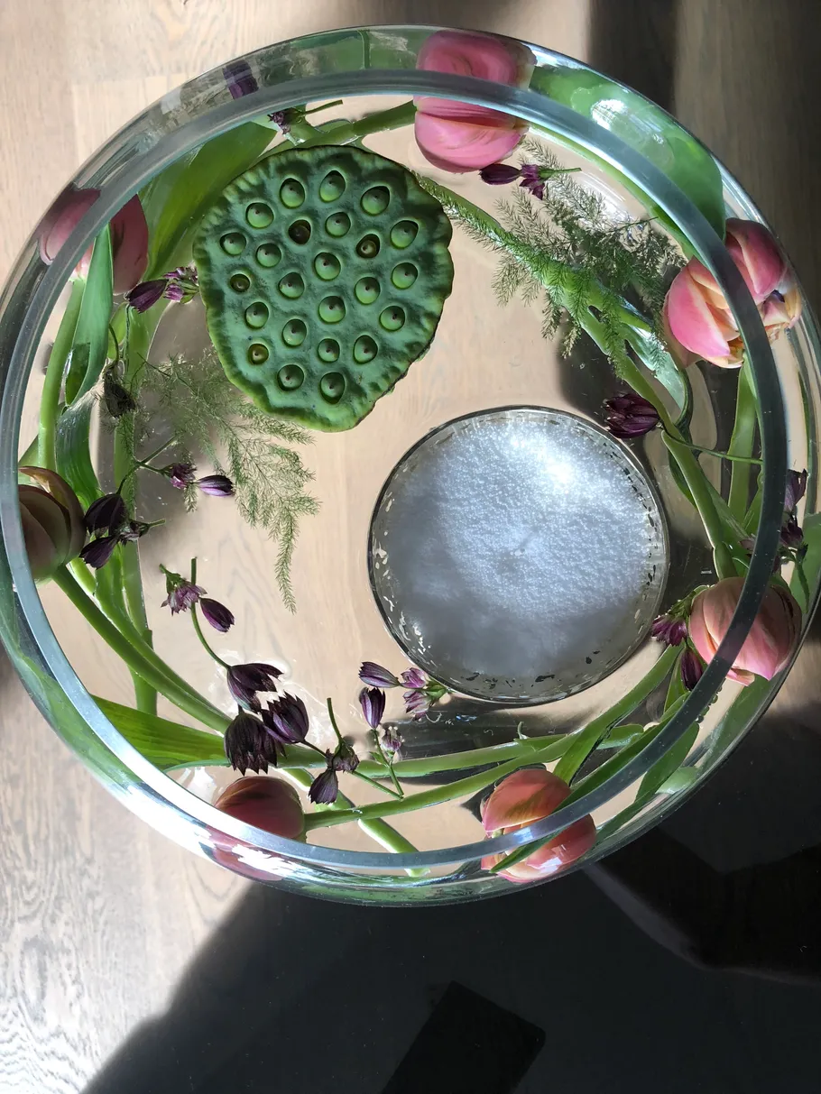 Glass bowl with flowers and greenery inside.