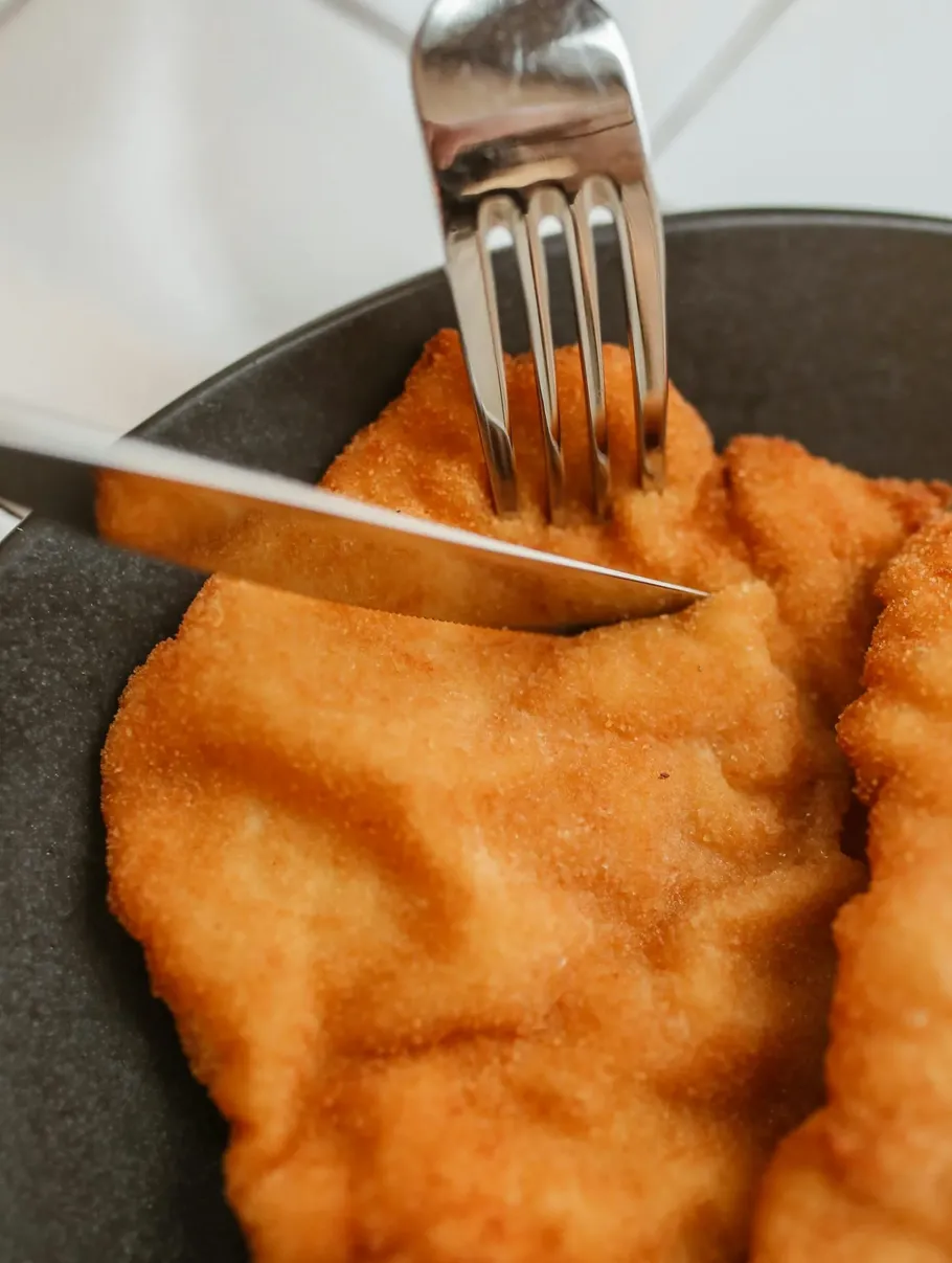 Gabel und Messer schneiden paniertes Fleisch auf Teller.