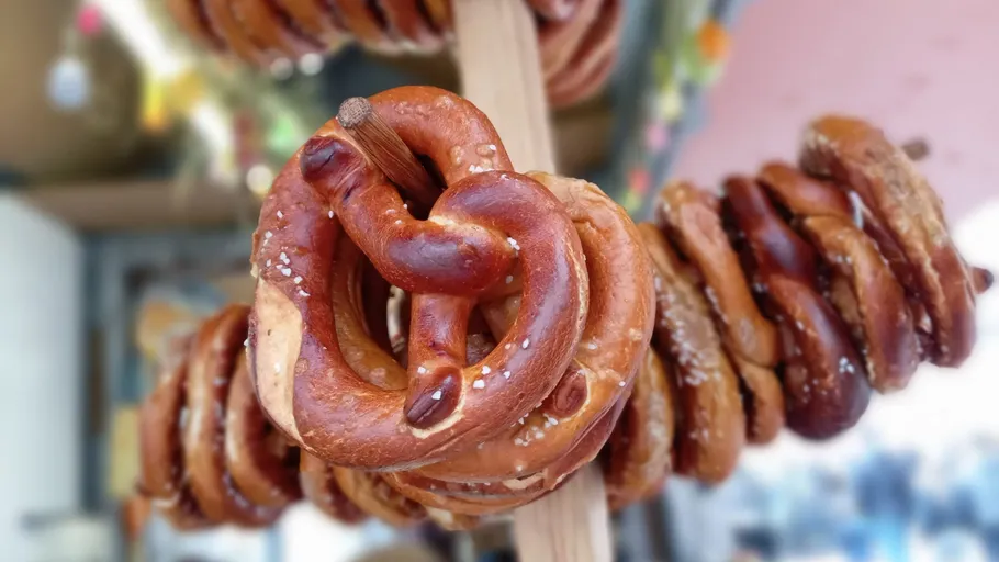 Pretzels hanging on a wooden stick outdoors.