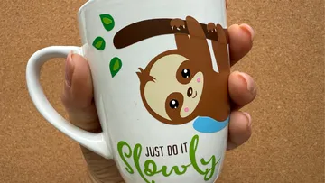 Hand hält Tasse mit Faultierdesign.