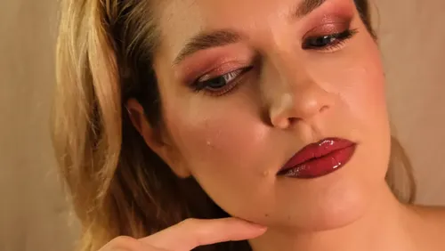 Woman with makeup, hand near chin, indoors.