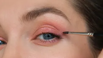 Eye with pink eyeshadow and makeup brush.
