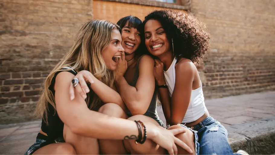 Three women sitting, smiling, against brick wall.