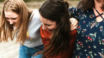 Drei Frauen lachen und umarmen sich draußen.