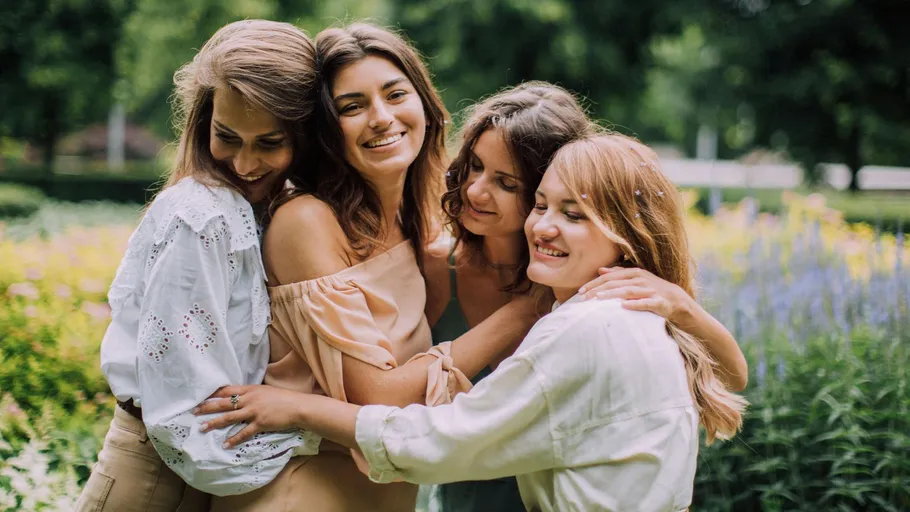 Four women hugging in a garden.