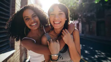 Two women smiling on a sunny street.