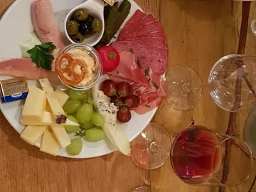 A plate of cheese, sausage, fruit and olives.