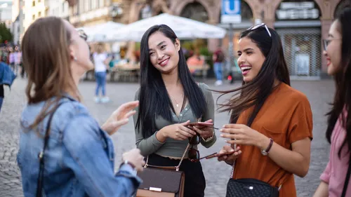 Four women smiling and talking in a plaza.