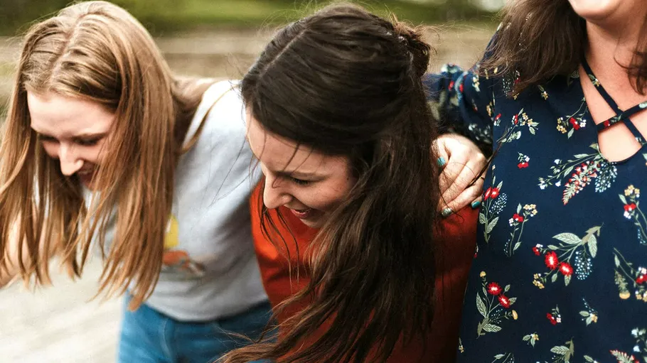 Drei lachende Frauen im Freien eng beieinander.