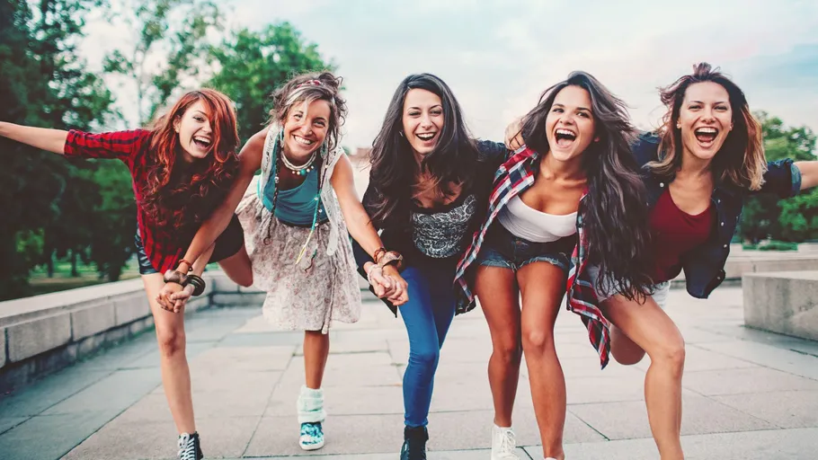 Five women laughing and posing outdoors.