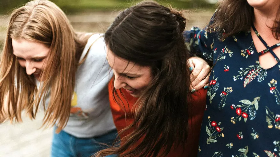 Drei lachende Frauen in enger Umarmung im Freien.