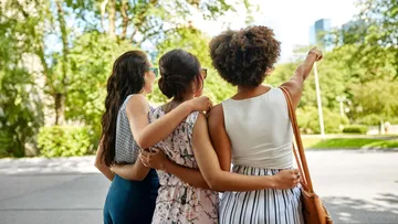 Three women embrace and point outside city.