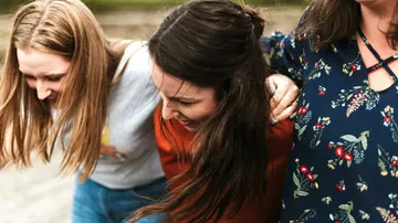 Drei Frauen lächelnd, Arme umeinander gelegt.