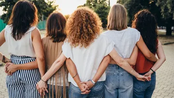 Fünf Frauen im Freien Arm in Arm stehend.