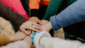 Hands stacked together in unity outdoors.