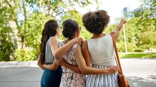 Three women hugging, pointing in park.